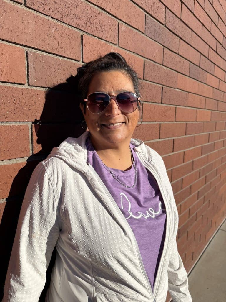 Smiling woman in sunglasses outside brick wall, promoting recovery and hope.